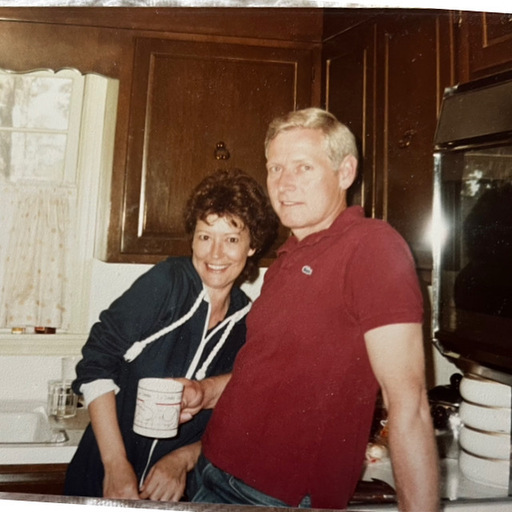 My deceased parents in approximately 1980, leaning on a kitchen counter, Dad has a coffee cup in hand. Mom leans into him. They are very young looking in their 40s, and handsome pair, he is fair, she is darker, brunette. 